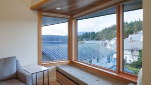 Una habitación con una banca empotrada y una pequeña mesa, ventanas amplias que dan a vistas de un lago y casas.