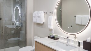 Un baño moderno con ducha de vidrio, inodoro, tocador con espejo y lavamanos.