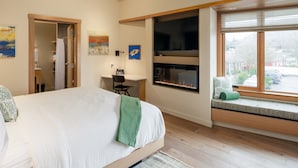 A modern bedroom with a large bed, a desk, a fireplace, and a window with a view of the outside. - Yellow - Comfortably Accessible (Eastsound)