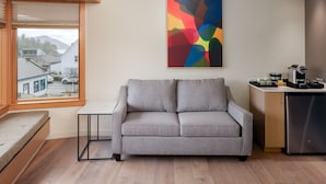 A modern living room with a grey sofa, a small table, and a kitchen area with a refrigerator. - Yellow - Comfortably Accessible (Eastsound)