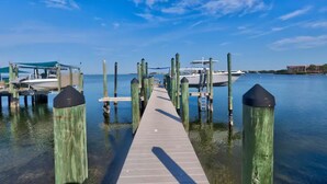 Un muelle de madera que conduce a un embarcadero con barcos, rodeado de aguas tranquilas y cielos despejados.