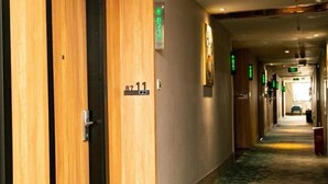 Un couloir d’hôtel avec des portes en bois, des panneaux indiquant le numéro des chambres et des panneaux de signalisation verts.