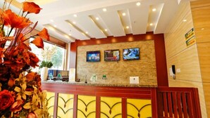 A hotel reception area with a wooden reception desk, a stone wall with three screens, and a floral arrangement on the left. - Greentree Inn Jiangsu Xuzhou Feng County Liubang Plaza Express Hotel (Xuzhou)