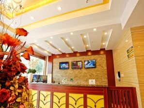 A hotel reception area with a wooden reception desk, a stone wall with three screens, and a floral arrangement on the left. - Greentree Inn Jiangsu Xuzhou Feng County Liubang Plaza Express Hotel (Xuzhou)