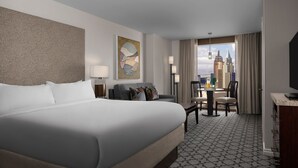 A hotel room with a large bed, a sofa, a desk, and a view of a cityscape.