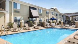 A swimming pool with lounge chairs and umbrellas, surrounded by a building with multiple windows and a covered patio area. - Quality Inn Ruston (Ruston)