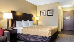 A hotel room with a large bed, two bedside lamps, a desk with a telephone, a chair, and a door. - Quality Inn Ruston (Ruston)