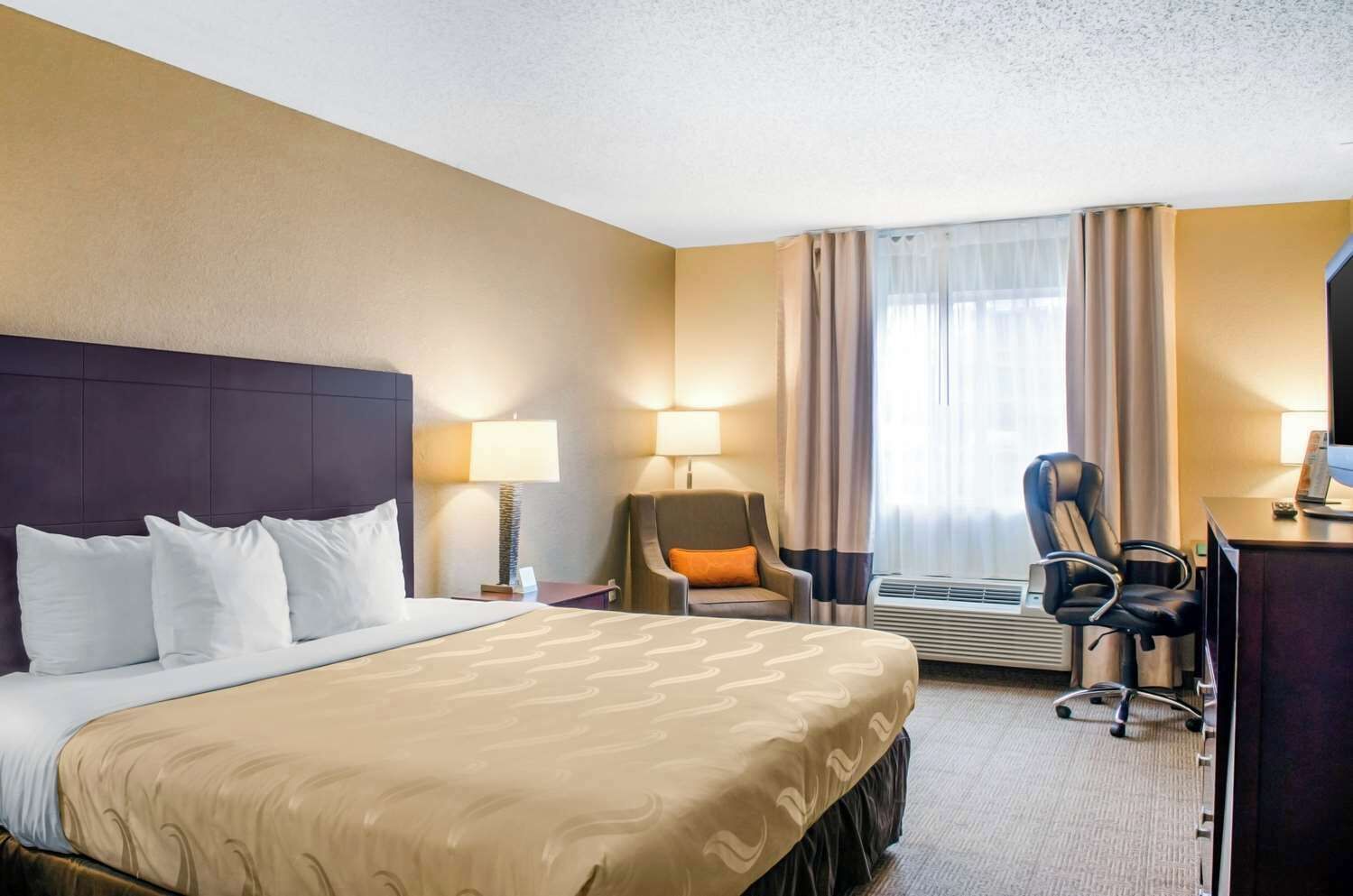 Habitación de hotel con una cama grande, dos sillones, un escritorio y una ventana con cortinas.