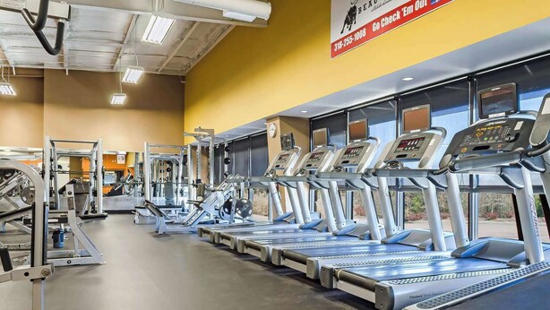 A gym with multiple treadmills, weight machines, and a yellow wall with a sign. - Quality Inn Ruston (Ruston)