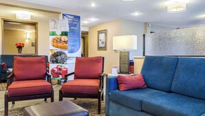 A hotel lobby with two red armchairs, a blue sofa, a small table with a lamp, and a banner advertising breakfast. - Quality Inn Ruston (Ruston)