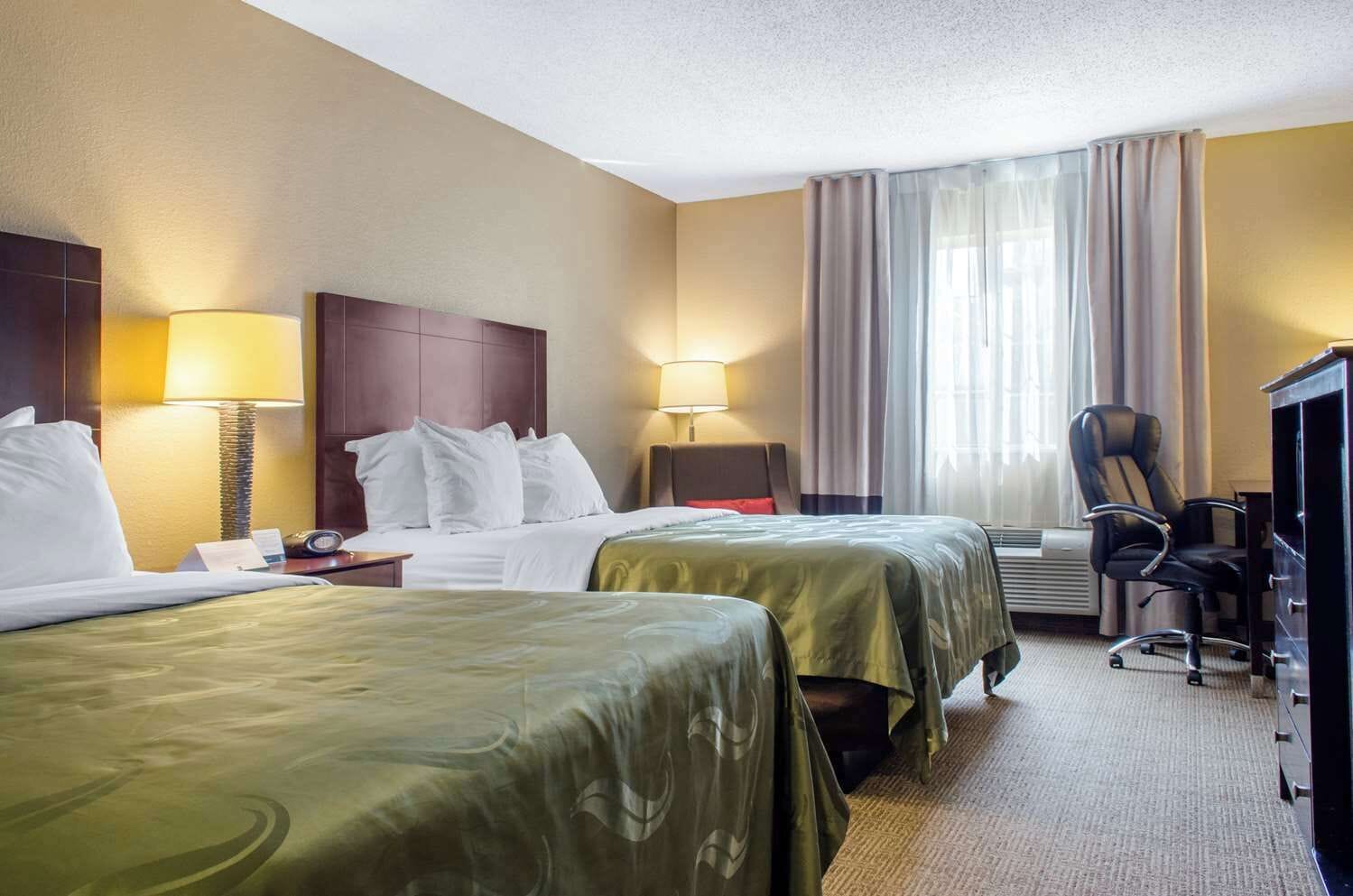 Habitación de hotel con dos camas, un escritorio, una silla y un televisor.