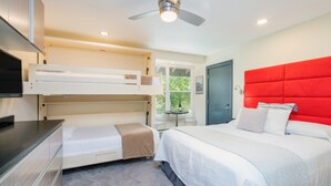 A bedroom with a bunk bed, a single bed, a red headboard, a ceiling fan, and a window with a view of greenery. - Mountainside Inn 421 1 Bedroom Hotel Room by Alpine Lodging Telluride (Telluride)