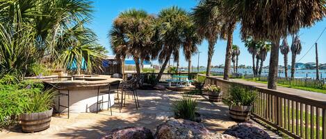 A patio area with outdoor seating, palm trees, and a view of the water.