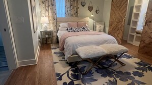 A bedroom with a bed, a nightstand, a lamp, a ceiling fan, and a large floral rug.