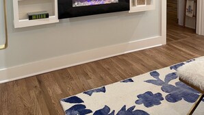 A living room with a fireplace, a flat-screen TV mounted above it, and a wooden floor.
