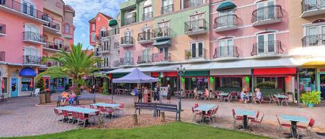 A courtyard with outdoor seating, surrounded by colorful buildings with balconies.