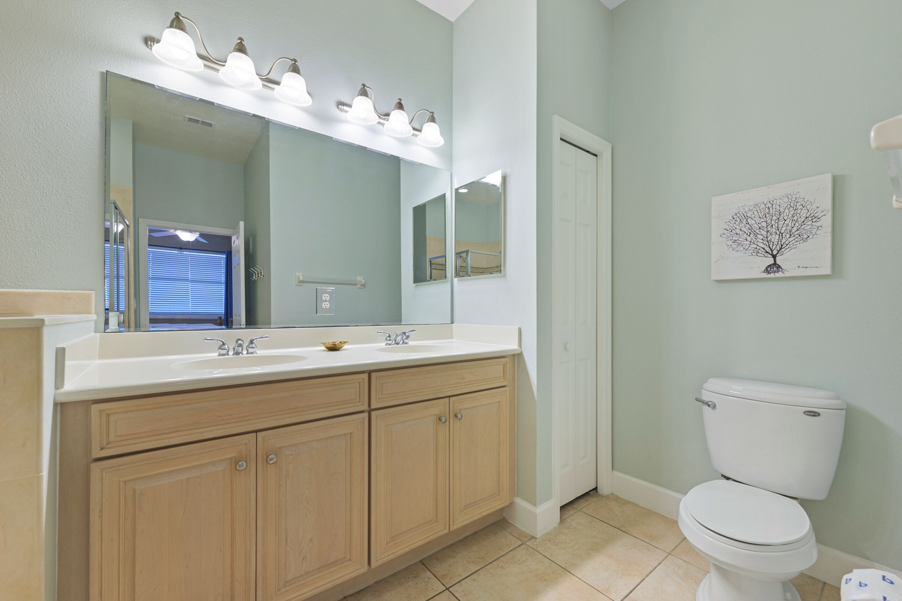 A bathroom with a large mirror, a sink with a vanity, a toilet, and a wall-mounted light fixture.