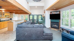 A spacious living area with a large gray sectional sofa, a fireplace, a television, and a kitchen with wooden cabinets and a bar area. - Mountainside Inn 101 2 Bedroom Condo by Alpine Lodging Telluride (Telluride)