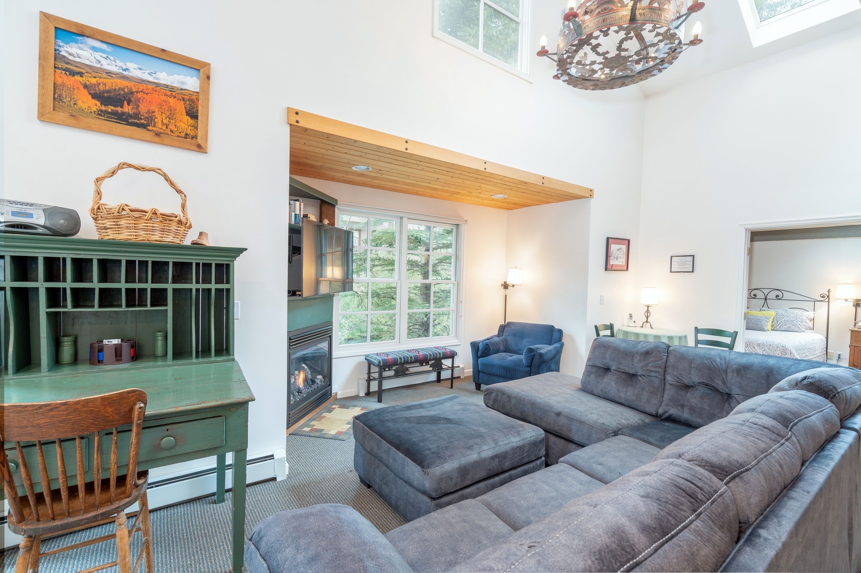 A cozy living room with a green desk, a blue armchair, a gray sofa, and a fireplace.