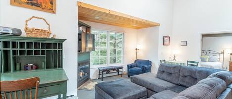 A cozy living room with a green desk, a blue armchair, a gray sofa, and a fireplace.