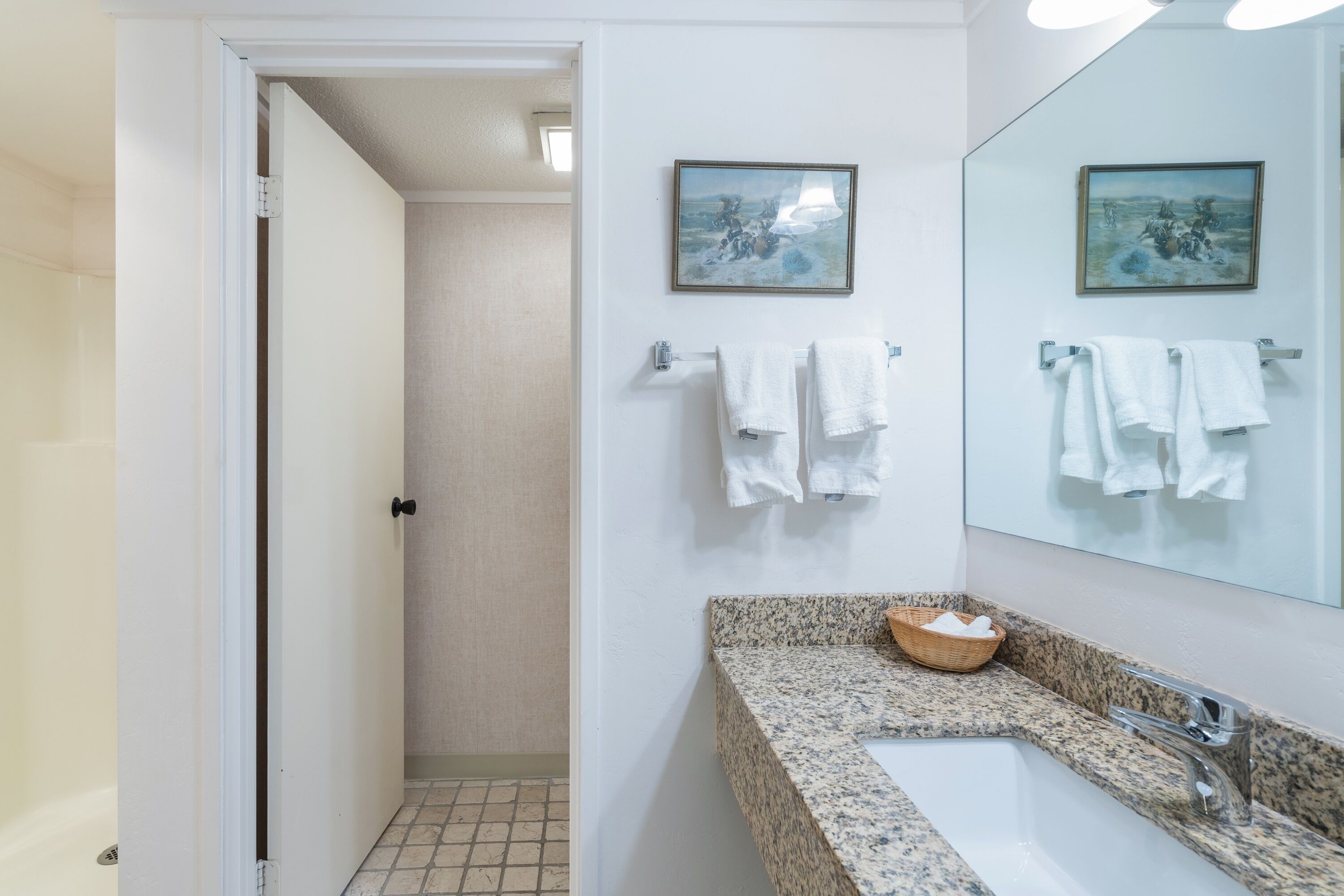 Une salle de bain avec un comptoir en granit, un lavabo et deux tableaux encadrés accrochés au mur.