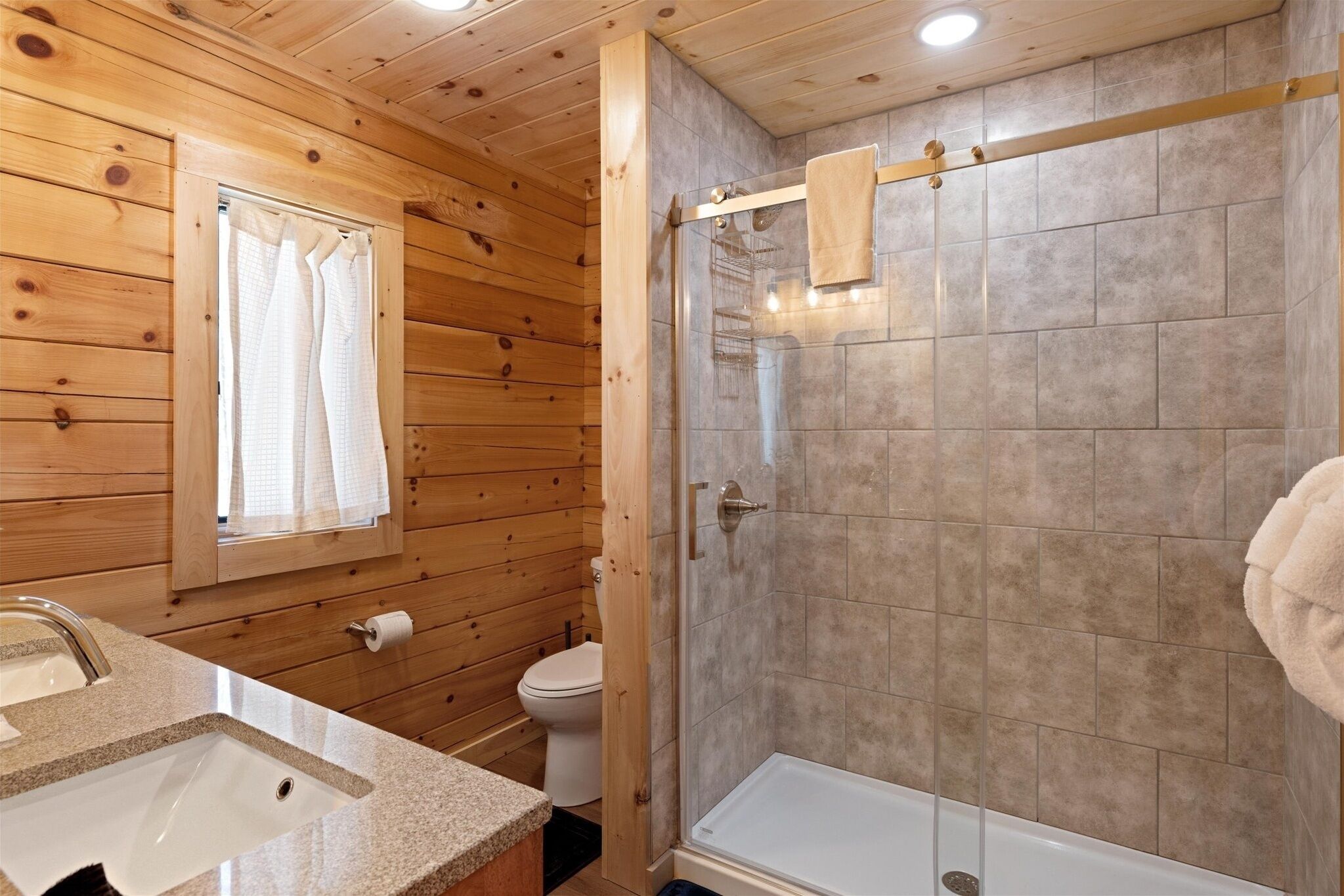 A wooden-paneled bathroom with a sink, toilet, and glass-enclosed shower.