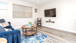 A living room with a blue sofa, a round coffee table, a TV mounted on the wall, and a wooden floor.