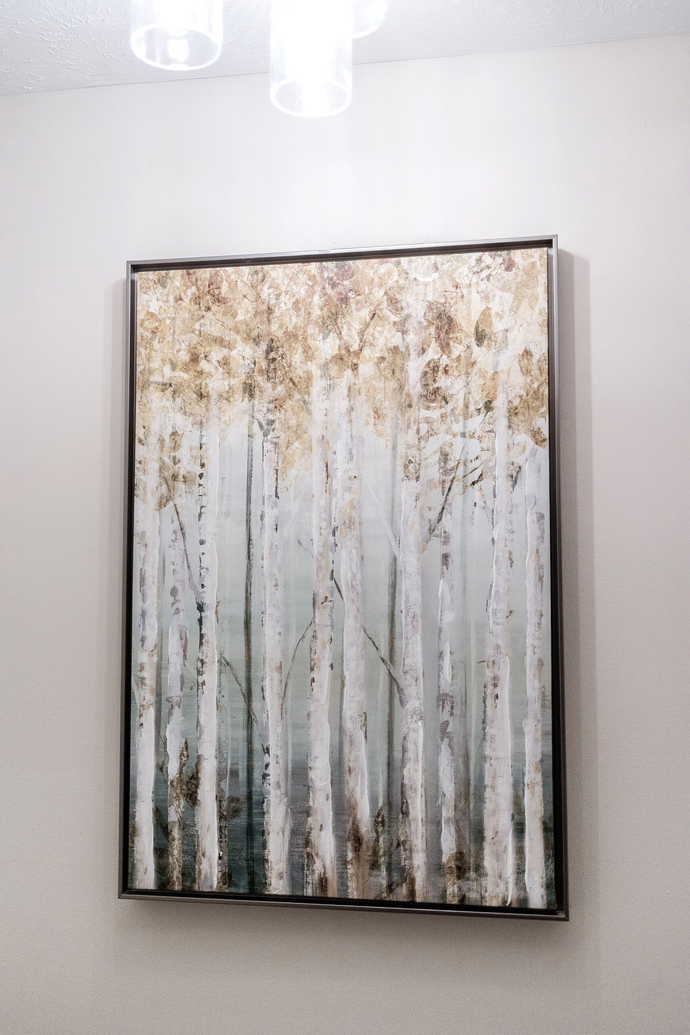 A framed artwork of birch trees on a plain wall.