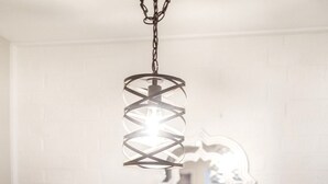 A dining area with a table, chairs, a hanging light fixture, and a decorative mirror on the wall.