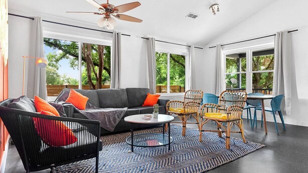 A modern living room with a sofa, chairs, a coffee table, and large windows offering a view of greenery outside.
