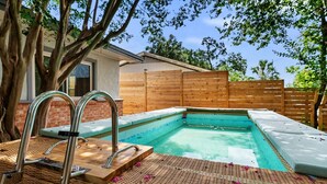 A rectangular swimming pool with a wooden deck and metal ladders, surrounded by a wooden fence and trees.