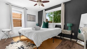 A bedroom with a bed, a ceiling fan, a window, a rug, and a nightstand with a lamp.