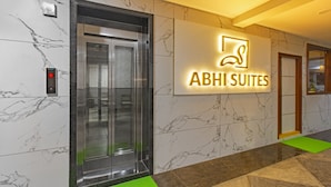 Un ascensor con pantalla digital, un letrero que dice 'ABHI SUITES' y una pared de mármol con un diseño geométrico en el suelo.