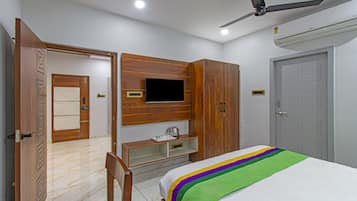 A bedroom with a bed, a TV mounted on the wall, a wardrobe, a desk, and a ceiling fan.