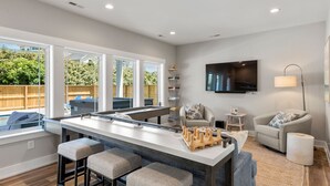 A modern kitchen with a large island, bar stools, a flat-screen TV, and a cozy seating area with a sofa and armchairs. - Osprey Isle: New Build | Private Pool | Rec Room (Corolla)