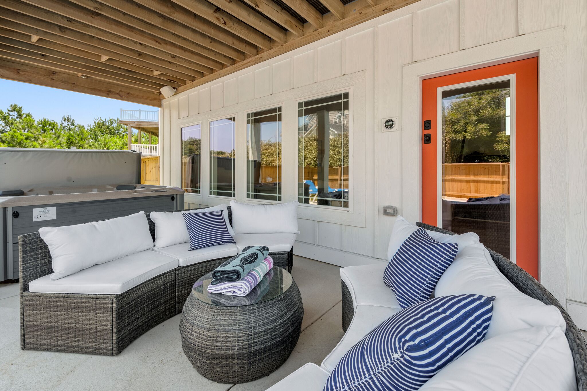 A covered outdoor seating area with wicker furniture and cushions, a glass table, and a red door.