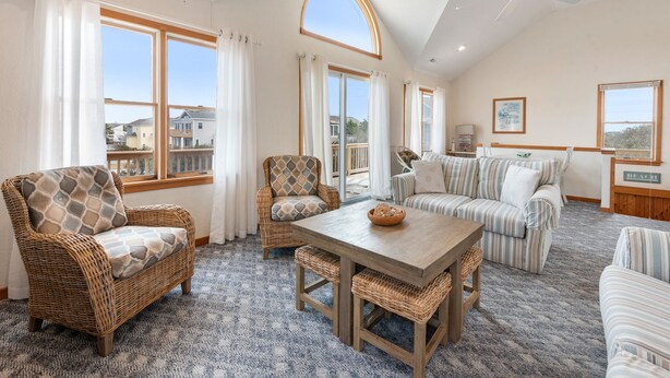 A spacious living room with a large wooden table, wicker chairs, and a striped sofa. - SomerVilla: Oceanside | Pool/Hot Tub | Pets OK (Corolla)