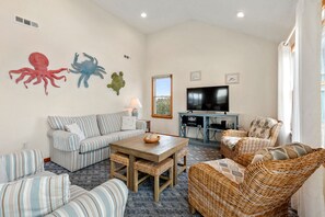 A living room with striped sofas, a wooden coffee table, wicker chairs, and a flat-screen TV.