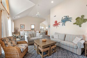 A spacious living room with a high ceiling, wicker furniture, striped sofas, and decorative wall art.
