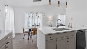 A modern kitchen with a central island, pendant lights, and a dining area with a table and chairs. - Luxury Home with Pool Near Disney & Theme Parks (Davenport)