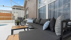 A modern outdoor seating area with a pool, a wooden fence, and a large window. - Luxury Home with Pool Near Disney & Theme Parks (Davenport)