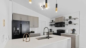 A modern kitchen with a central island, black appliances, and white cabinetry. - Luxury Home with Pool Near Disney & Theme Parks (Davenport)
