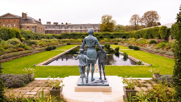 Une statue représentant un homme accompagné de deux enfants, dans un jardin à la française agrémenté d’un bassin et de pelouses parfaitement entretenues.