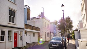 Une rue étroite bordée de bâtiments blancs et bleus, avec une porte rouge et des voitures garées.