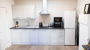 Une cuisine moderne avec des armoires blanches, un comptoir noir, une hotte de cuisinière en acier inoxydable, un four à micro-ondes et un réfrigérateur.