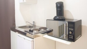 Eine kompakte Küchenzeile mit integriertem Mikrowellenherd, Kaffeemaschine und kleinem Kühlschrank.
