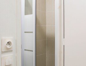 A bathroom with a white tiled wall, a white door, and a white switchboard. - Cozy studio in a quiet location – Paris 15th (Paris)