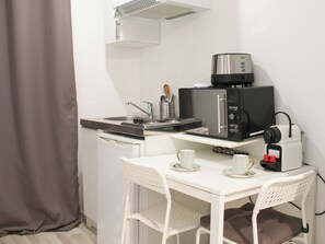 A compact kitchenette with a microwave, a small sink, and a white table with two cups.