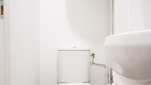 Ein kleines, sauberes Badezimmer mit Toilette, Waschbecken und weißen Fliesen.