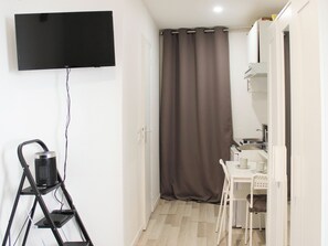 A small room with a television mounted on the wall, a white desk with a chair, and a curtain covering a door.